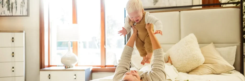Mother playing with baby on Amish-made bed